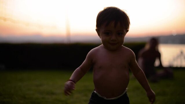 Latin shirtless baby boy walking on the grass having fun at dusk