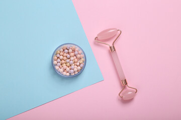 Facial massage roller and balls of powder on blue pink pastel background. Top view