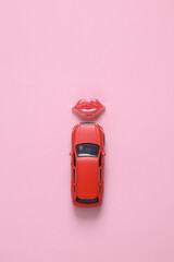 Model of a red car with lips on a pink background. Top view