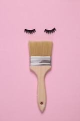 False eyelashes with a paint brush in the shape of face on pink background. Minimal layout