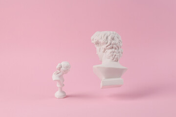 Levitating Antique Plaster busts of David and Venus on pink background with shadow. Conceptual pop....