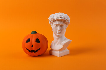 Plaster bust of David with jack lantern pumpkin head on orange background. Halloween concept. Minimal still life photo