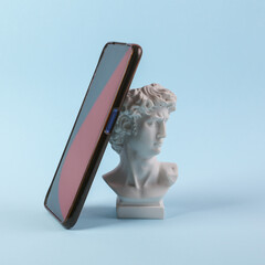 Antique bust of david with smartphone on blue background. Minimal still life. Concept art layout