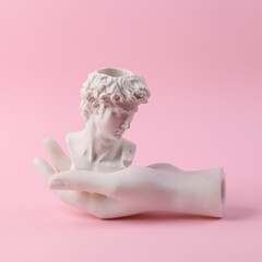 Antique bust of David with white hand on a pink background. Minimal still life