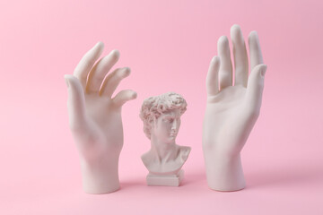 Antique bust of David with statues of hands on a pink background. Minimal still life