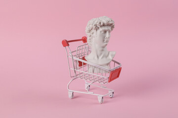 Antique bust of David with shopping trolley on a pink background. Conceptual pop. Minimal shopping...