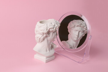 Bust of David admires himself looking in a mirror on a pink background. Narcissism. Minimal still...
