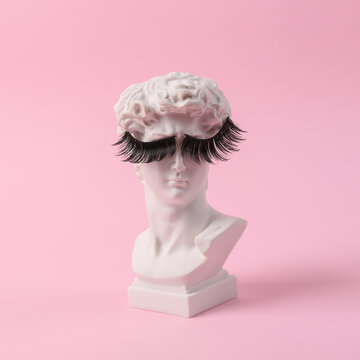 Antique bust of David with false eyelashes on a pink background. Conceptual pop. Minimal beauty and fashion still life. Creative idea