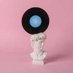 Antique bust of David with vinyl record on pink background. Conceptual pop. Minimal 70s still life....