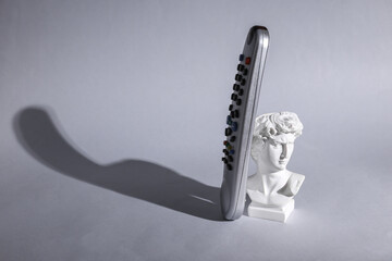 David's bust with tv remote on gray background with long shadow. Minimal still life