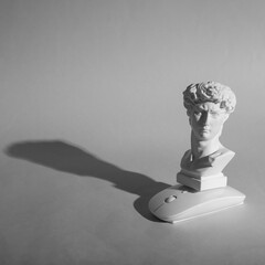 Antique bust of David with modern pc mouse on gray background. Minimal still life