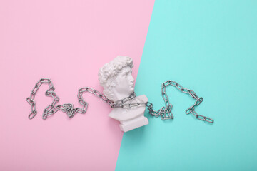 Antique bust of David wrapped steel chain on turquoise pink background. Conceptual pop. Minimal...