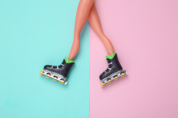 Doll legs with roller skates on blue-pink pastel background. Top view. Flat lay
