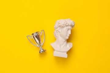 David bust with winner cup on yellow background. Minimal still life photo