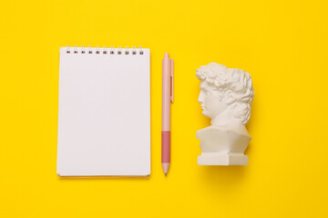 David bust with notebook on yellow background. Minimal still life photo