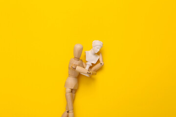Wooden puppet holding venus bust on yellow background