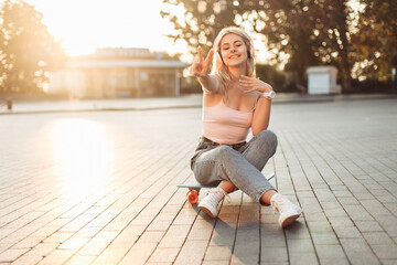 Fototapeta na wymiar Young smiling cool girl sitting on skateboard in the city