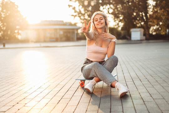 Young smiling cool girl sitting on skateboard in the city