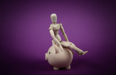 Wooden puppet sitting on piggy bank on a purple background. Save money concept
