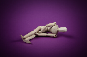 Scared or stressed wooden puppet lies on purple background