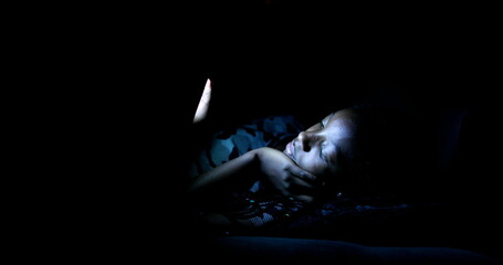 Teen girl using smartphone at night in the dark. African black ethnicity