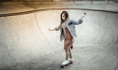 Cheerful extraordinary millennial woman with bright makeup and African braids is riding a penny board in a skatepark