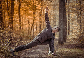 Active sport man trains warm-up exercises or stretching in the autumn forest. Healthy lifestyle. Outdoor workout