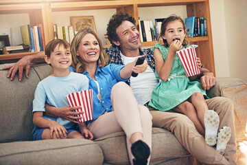 Movie night is their favourite family tradition. Shot of a happy family watching movies on the sofa...