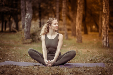 Attractive Caucasian yogi woman sitting on a mat on the grass. Healthy lifestyle