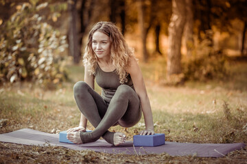 Curly yogi woman exercising with exercise bricks in the forest