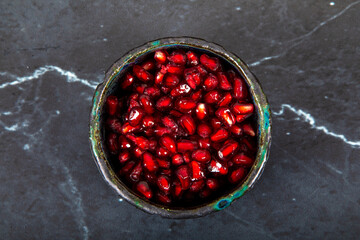 pomegranate in bowl isolated on black. Top view, space for text.
