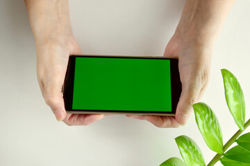 Close-up of an elderly woman holding a mobile phone with a horizontal green screen on a light table