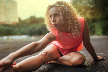 A young curly blonde of athletic build performs a warm-up before training at the stadium. Outdoor...