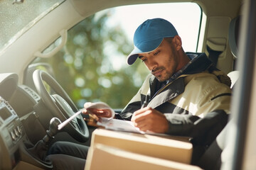 Updating his delivery status. Shot of a delivery man reading addresses while sitting in a delivery...