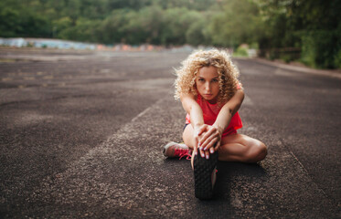 A young curly blonde of athletic build performs a warm-up before training at the stadium. Outdoor...