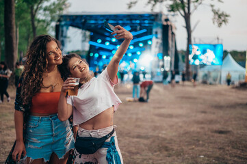 Two beautiful friends taking a selfie with a smartphone on a music festival