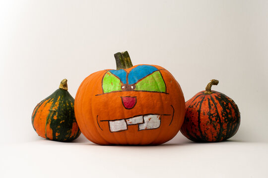 Halloween decorated big boss orange pumpkin with painted angry face in the middle between two little not painted pumpkins orange and green with white isolated background.