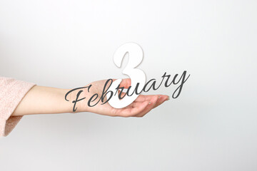 February 3rd. Day 3 of month, Calendar date. Calendar Date floating over female hand on grey background. Winter month, day of the year concept.