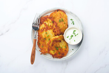 Potato pancakes. Fried homemade potato pancakes or latkes with cream and green onions in rustic plate on white marble table background. Rustic style. Healthy food. Top view.