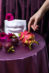 Creative modern still life made against purple satin with flowers and exotic fruits - pitahaya, mangosteen.