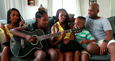 Happy African family enjoying music. Teen daughter playing guitar for parents and siblings