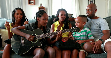 Happy African family enjoying music. Teen daughter playing guitar for parents and siblings