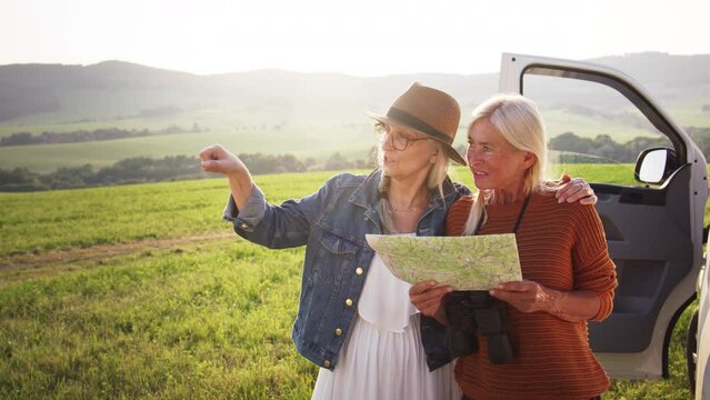 Senior women friends using map outdoors in nature, caravan trip holiday.