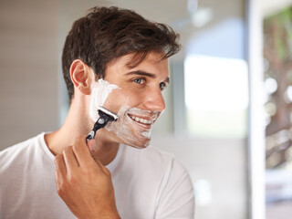 Enjoying his morning routine. Cropped shot of a young man shaving his facial hair with a disposable...