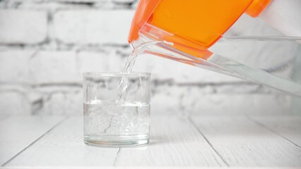 Pouring clear water from filter pitcher in glass on white background. Clean filtered water from jug. Concept of benefits of drinking regime and human health. Drink liquid every day