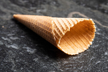 Empty crispy ice cream waffle cone on black lying on a black stone or table