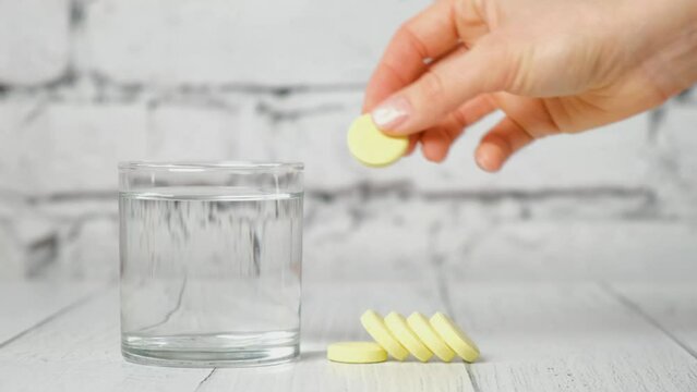 hand holds yellow effervescent soluble tablet and places it in glass of water. Concept of treatment and prevention of viral diseases. Help for depression and insomnia. white background. slow motion.