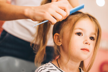 Fototapeta premium Stylish little girl in a beauty salon for children where she made a beautiful hairstyle. Female stylist makes stylish hairstyle to little girl.