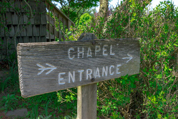 An old wooden chapel entrance sign with arrows