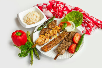 Selection of BBQ chicken tikka and seekh kebabs served with rice salad in a dish isolated on colorful table cloth top view on grey background